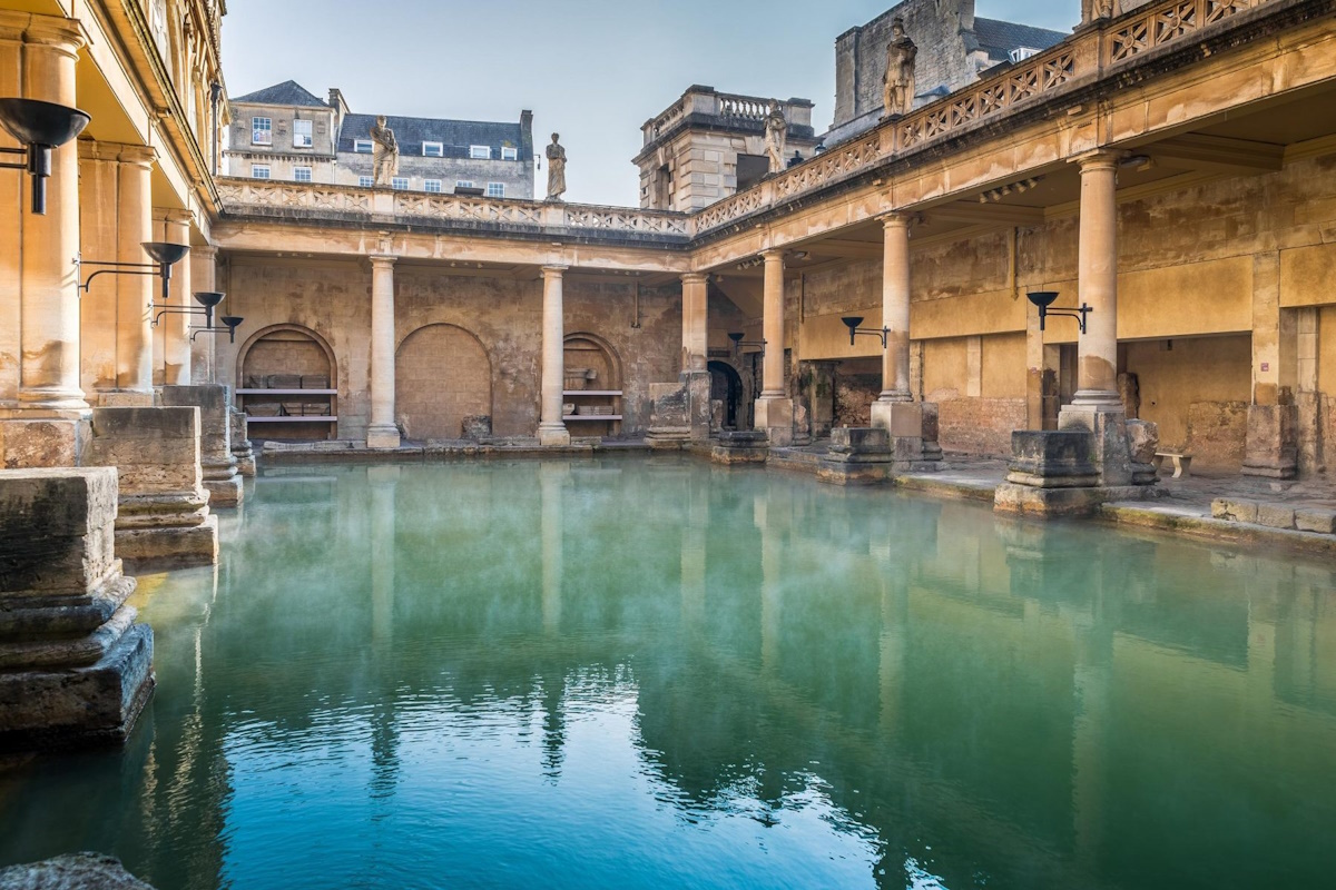 Main pool of the Roman Baths with green water and Roman statues